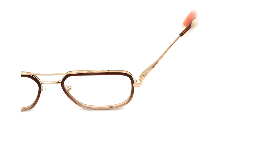 A close-up side view of a pair of eyeglasses with a gold metal frame and brown acetate trim, featuring a thin temple arm with a pink and white tip, set against a plain white background.