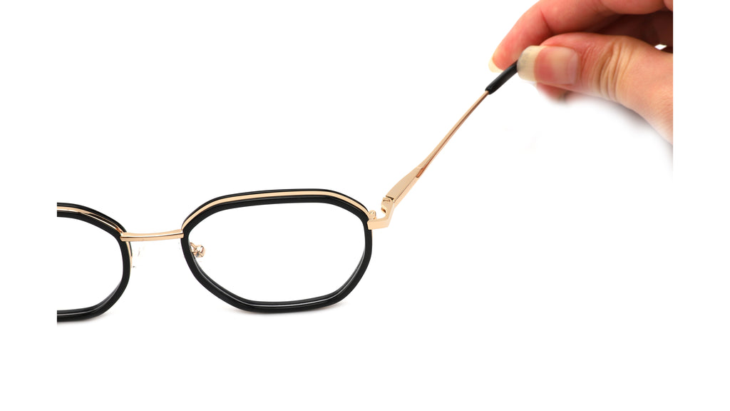 Oval eyeglasses with a black front and gold metal arms, shown with a hand holding one temple arm against a white background.
