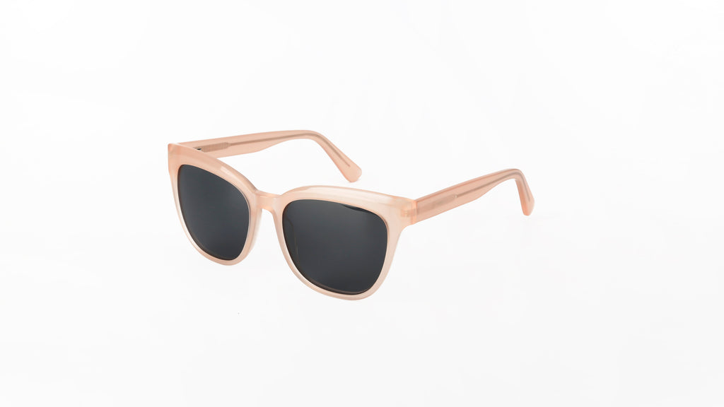 A pair of sunglasses with a translucent light pink acetate frame and dark gray lenses, shown on a plain white background.